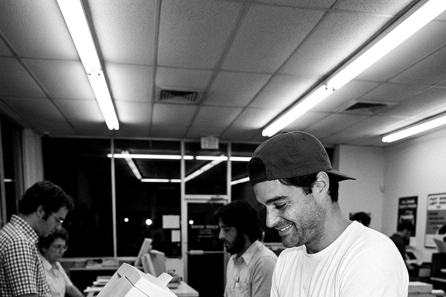 Hunter Siegel stands at a self-service copier inside a print shop before dawn, a stack of freshly printed pages on the counter beside him.