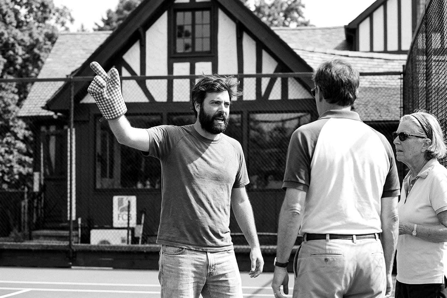 Andrew Simone stands outside the Rowayton hut in daylight, one hand gloved in an oven mitt, gesturing toward two men listening nearby.